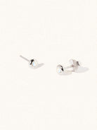 A pair of sterling silver small stud earrings with a 3mm moonstone gemstone in a 4mm setting and butterfly fastening. Set on a cream background with gentle shadowing.