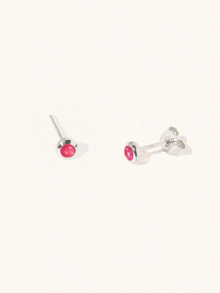 A pair of sterling silver small stud earrings with a 3mm ruby quartz gemstone in a 4mm setting and butterfly fastening. Set on a cream background with gentle shadowing.