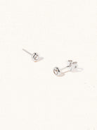 A pair of sterling silver small stud earrings with a 3mm white topaz gemstone in a 4mm setting and butterfly fastening. Set on a cream background with gentle shadowing.