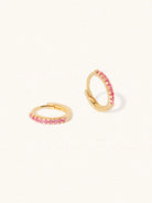 A pair of gold plated huggies with 10 Pink Quartz gemstones per huggie. Set on a cream background with elongated shadows