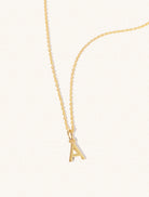 A gold chain necklace with the caplital letter A approximately 8mm x 6mm. Set on a cream background with gentle shadowing.