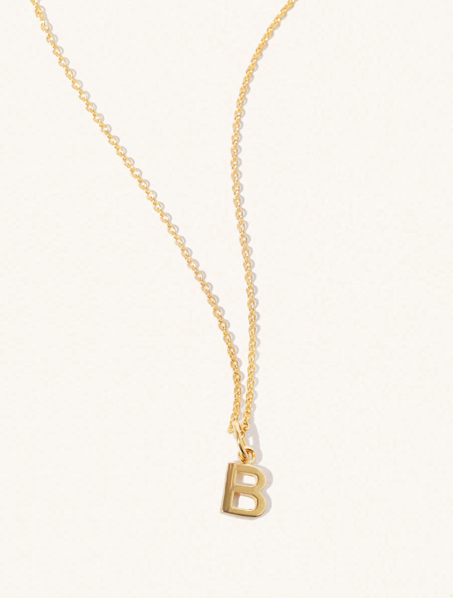 A gold chain necklace with the caplital letter B approximately 8mm x 6mm. Set on a cream background with gentle shadowing.