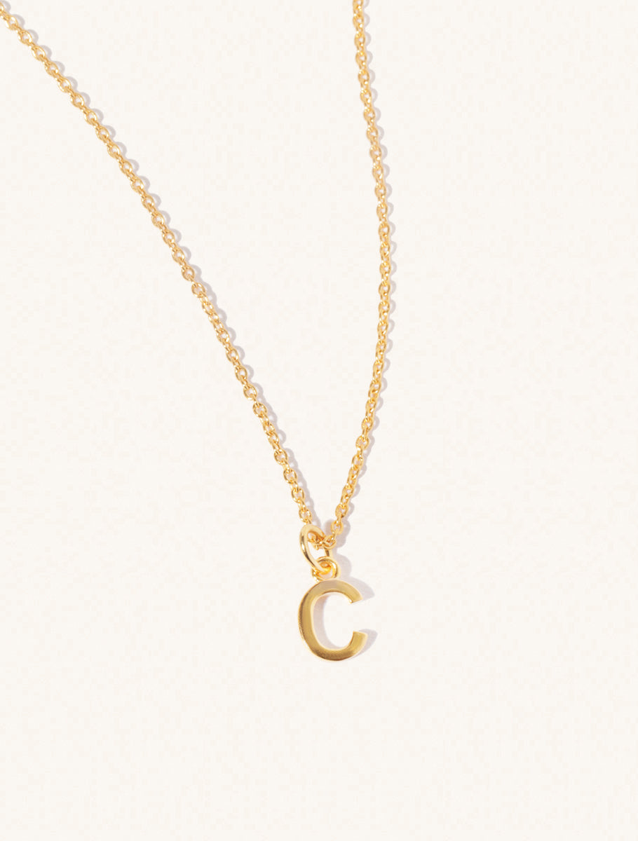 A gold chain necklace with the caplital letter C approximately 8mm x 6mm. Set on a cream background with gentle shadowing.