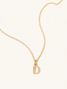 A gold chain necklace with the caplital letter D approximately 8mm x 6mm. Set on a cream background with gentle shadowing.