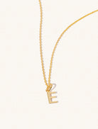 A gold chain necklace with the caplital letter E approximately 8mm x 6mm. Set on a cream background with gentle shadowing.