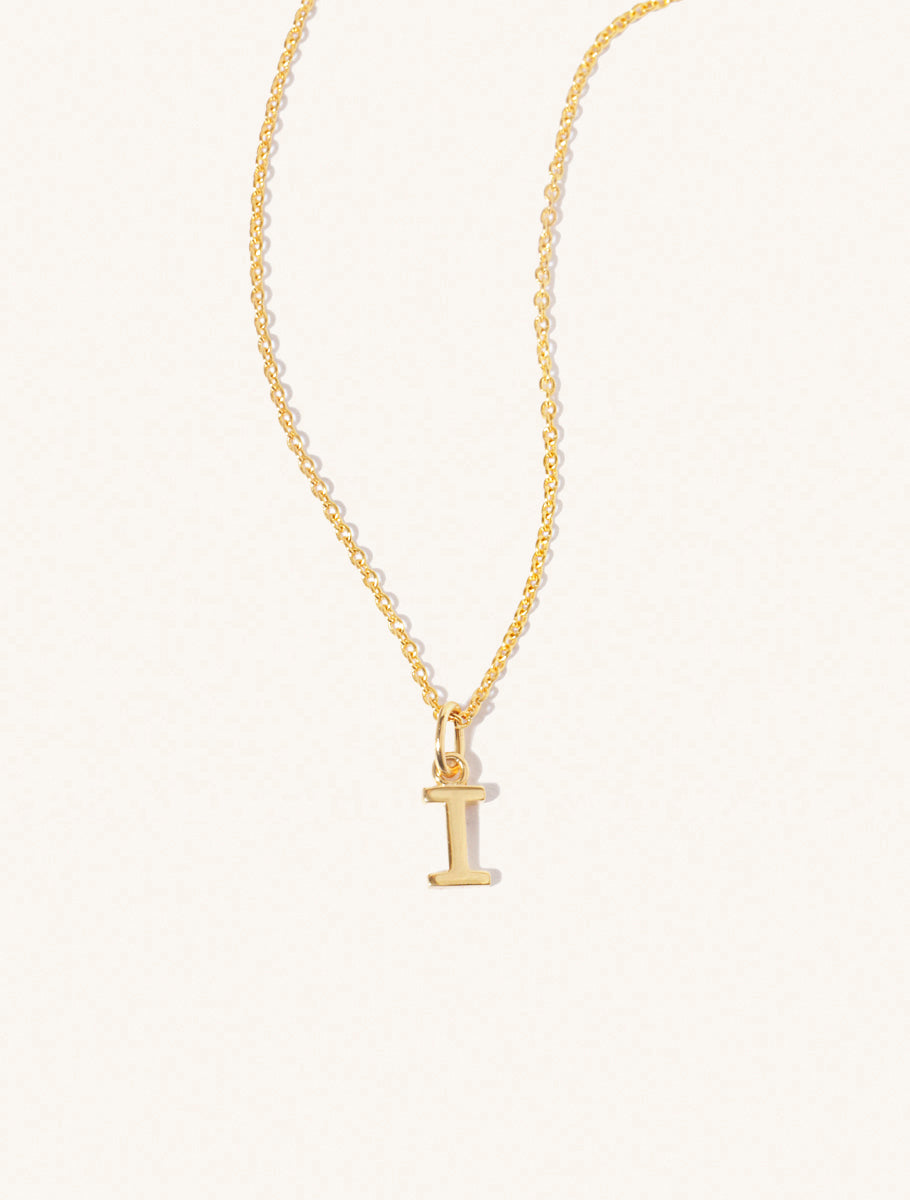 A gold chain necklace with the caplital letter I approximately 8mm x 6mm. Set on a cream background with gentle shadowing.