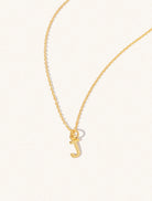 A gold chain necklace with the caplital letter J approximately 8mm x 6mm. Set on a cream background with gentle shadowing.