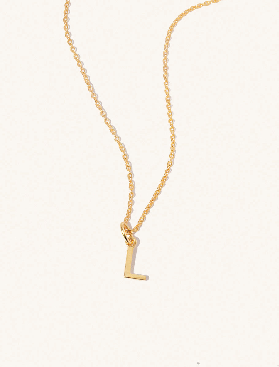 A gold chain necklace with the caplital letter L approximately 8mm x 6mm. Set on a cream background with gentle shadowing.