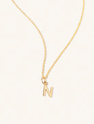 A gold chain necklace with the caplital letter N approximately 8mm x 6mm. Set on a cream background with gentle shadowing.