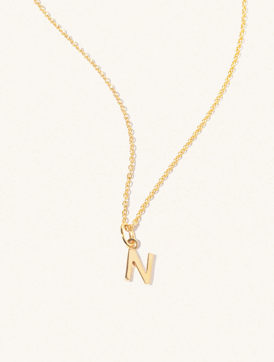 A gold chain necklace with the caplital letter N approximately 8mm x 6mm. Set on a cream background with gentle shadowing.