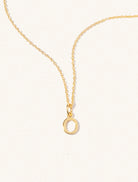 A gold chain necklace with the caplital letter O approximately 8mm x 6mm. Set on a cream background with gentle shadowing.