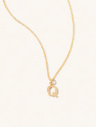 A gold chain necklace with the caplital letter Q approximately 8mm x 6mm. Set on a cream background with gentle shadowing.