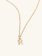 A gold chain necklace with the caplital letter R approximately 8mm x 6mm. Set on a cream background with gentle shadowing.