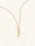 A gold chain necklace with the caplital letter T approximately 8mm x 6mm. Set on a cream background with gentle shadowing.