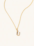 A gold chain necklace with the caplital letter U approximately 8mm x 6mm. Set on a cream background with gentle shadowing.