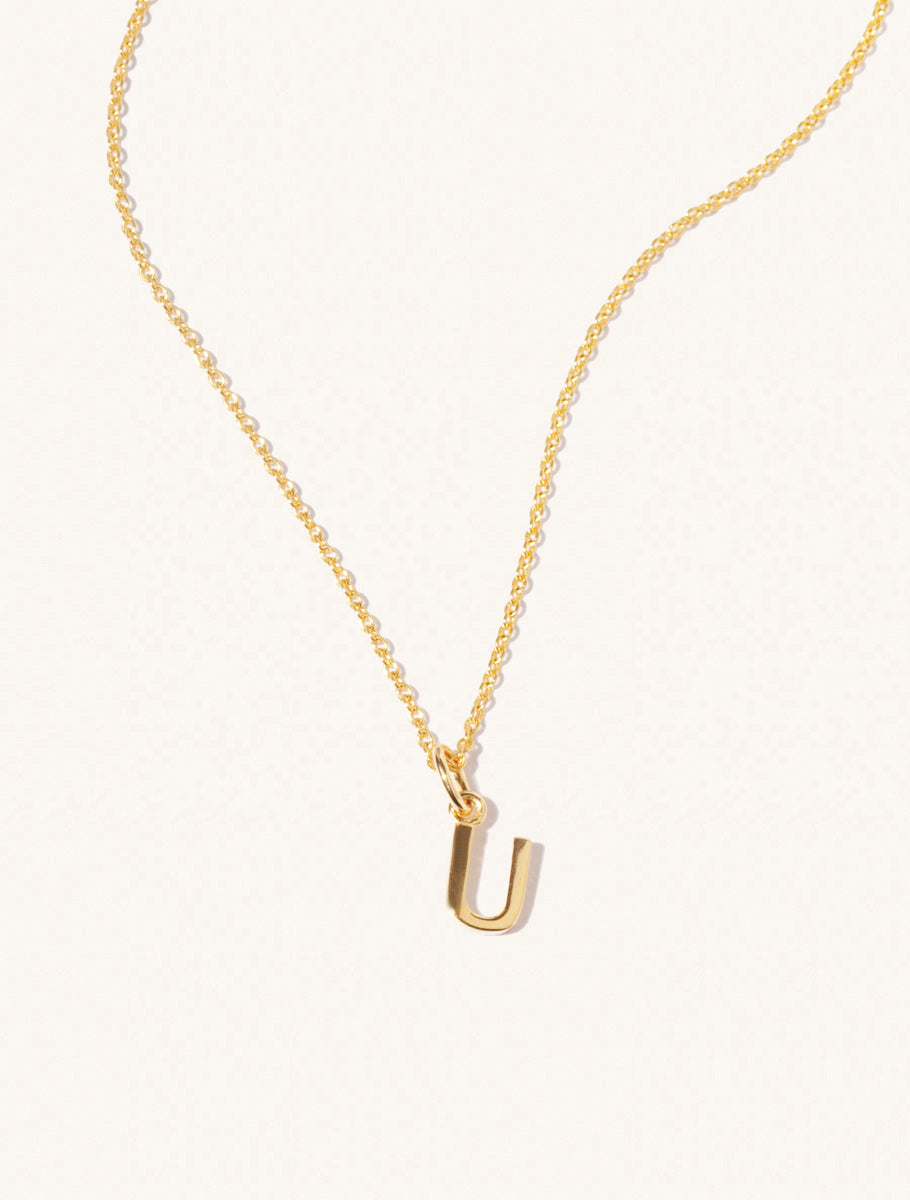 A gold chain necklace with the caplital letter U approximately 8mm x 6mm. Set on a cream background with gentle shadowing.