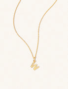 A gold chain necklace with the caplital letter W approximately 8mm x 6mm. Set on a cream background with gentle shadowing.