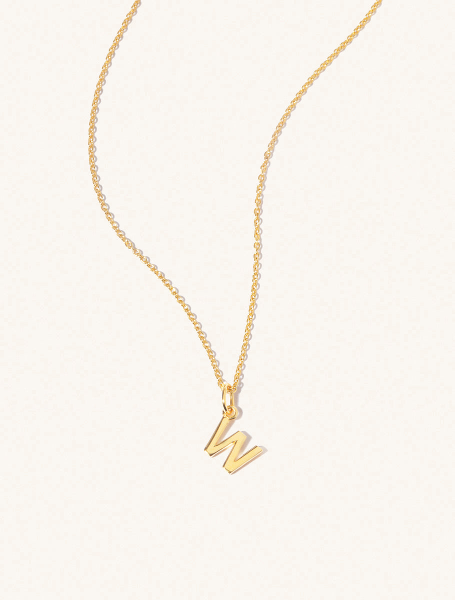 A gold chain necklace with the caplital letter W approximately 8mm x 6mm. Set on a cream background with gentle shadowing.