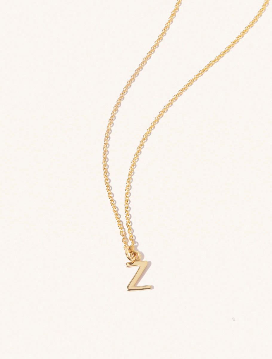 A gold chain necklace with the caplital letter Z approximately 8mm x 6mm. Set on a cream background with gentle shadowing.