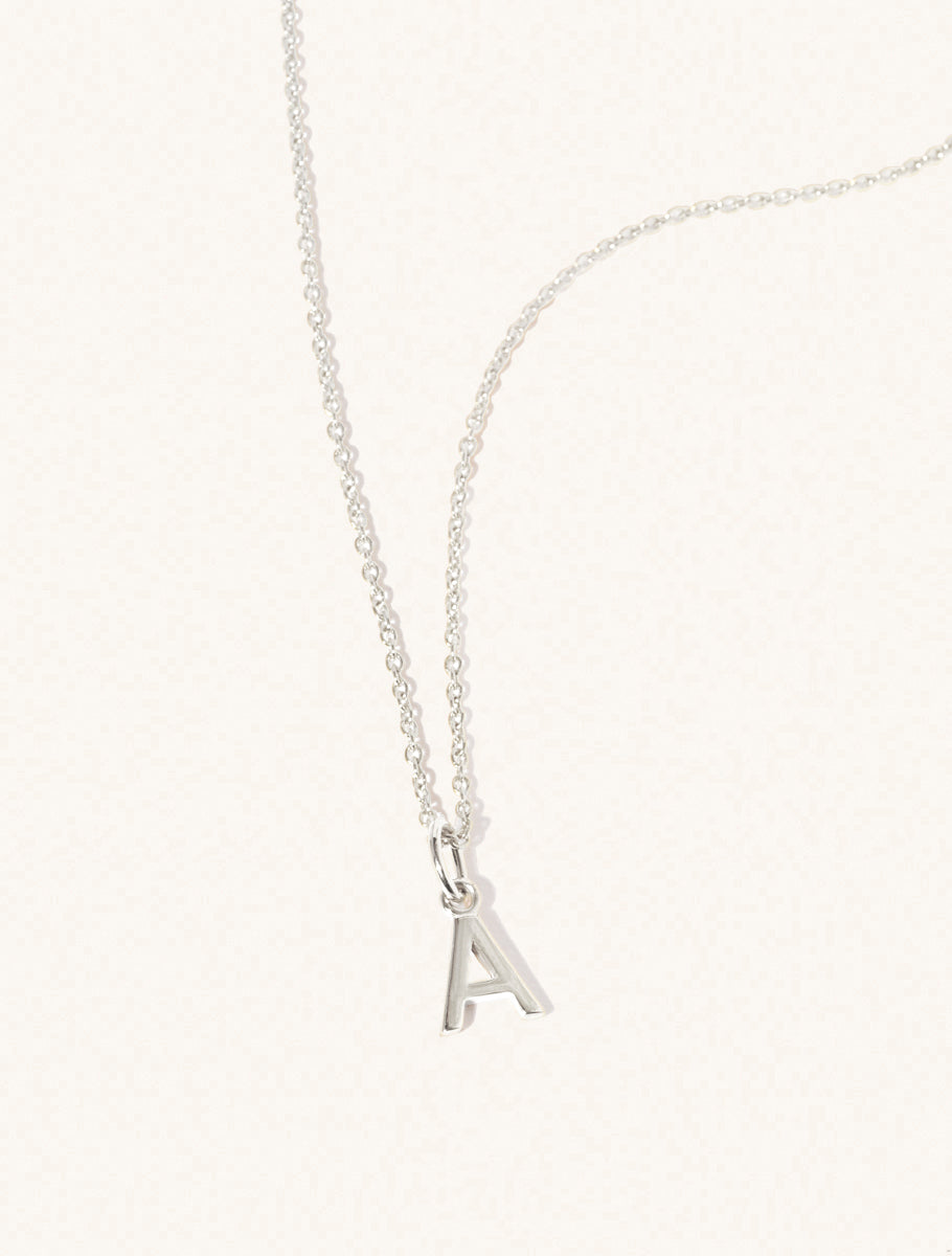 A sterling silver chain necklace with the caplital letter A approximately 8mm x 6mm. Set on a cream background with gentle shadowing.