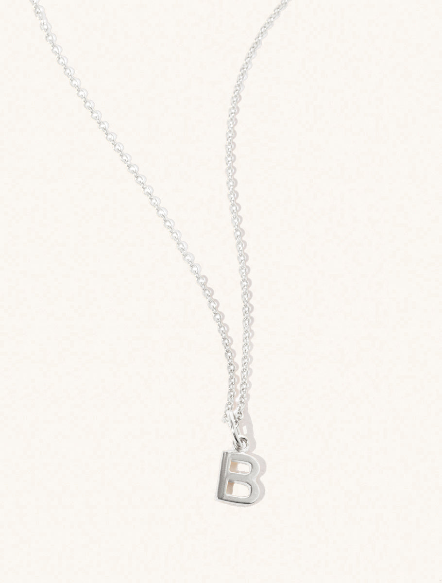 A sterling silver chain necklace with the caplital letter B approximately 8mm x 6mm. Set on a cream background with gentle shadowing.