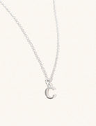 A sterling silver chain necklace with the caplital letter C approximately 8mm x 6mm. Set on a cream background with gentle shadowing.