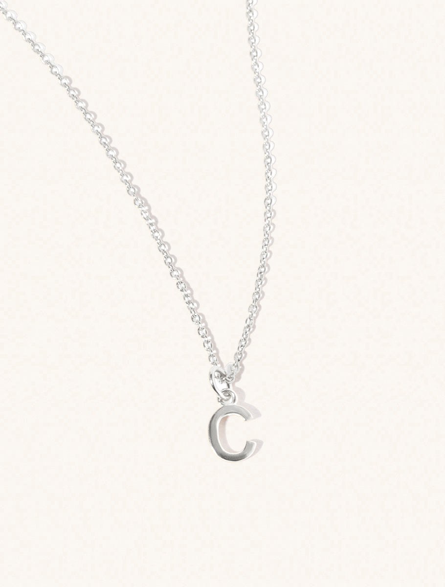 A sterling silver chain necklace with the caplital letter C approximately 8mm x 6mm. Set on a cream background with gentle shadowing.