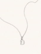 A sterling silver chain necklace with the caplital letter D approximately 8mm x 6mm. Set on a cream background with gentle shadowing.