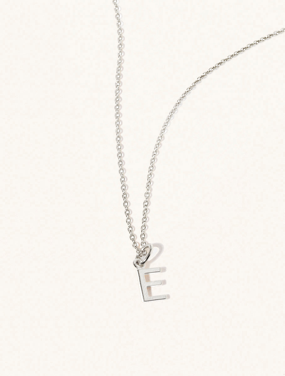 A sterling silver chain necklace with the caplital letter E approximately 8mm x 6mm. Set on a cream background with gentle shadowing.