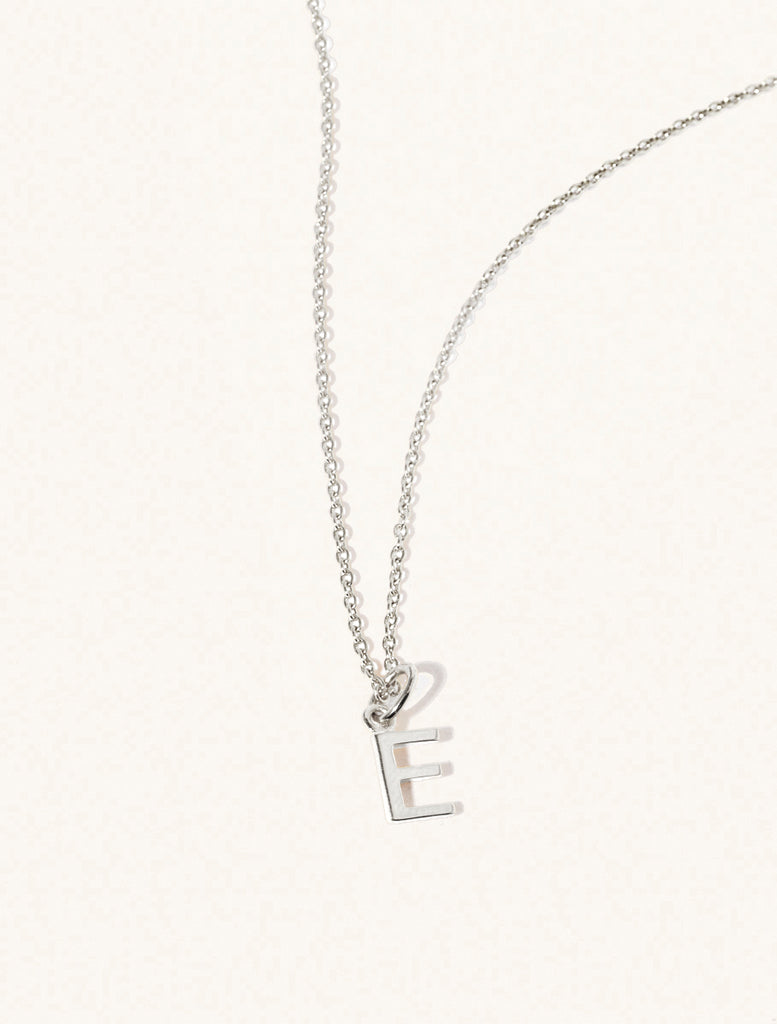 A sterling silver chain necklace with the caplital letter E approximately 8mm x 6mm. Set on a cream background with gentle shadowing.