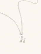 A sterling silver chain necklace with the caplital letter H approximately 8mm x 6mm. Set on a cream background with gentle shadowing.