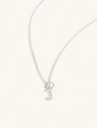 A sterling silver chain necklace with the caplital letter J approximately 8mm x 6mm. Set on a cream background with gentle shadowing.