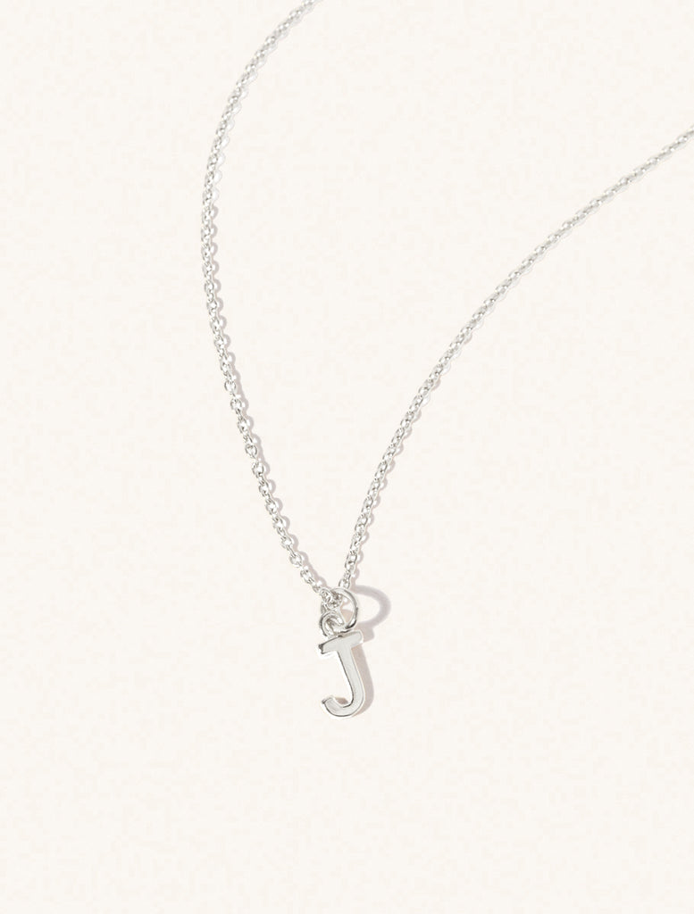 A sterling silver chain necklace with the caplital letter J approximately 8mm x 6mm. Set on a cream background with gentle shadowing.