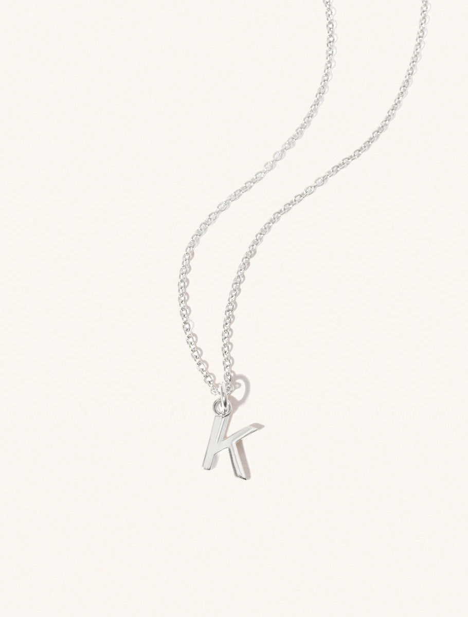 A sterling silver chain necklace with the caplital letter K approximately 8mm x 6mm. Set on a cream background with gentle shadowing.