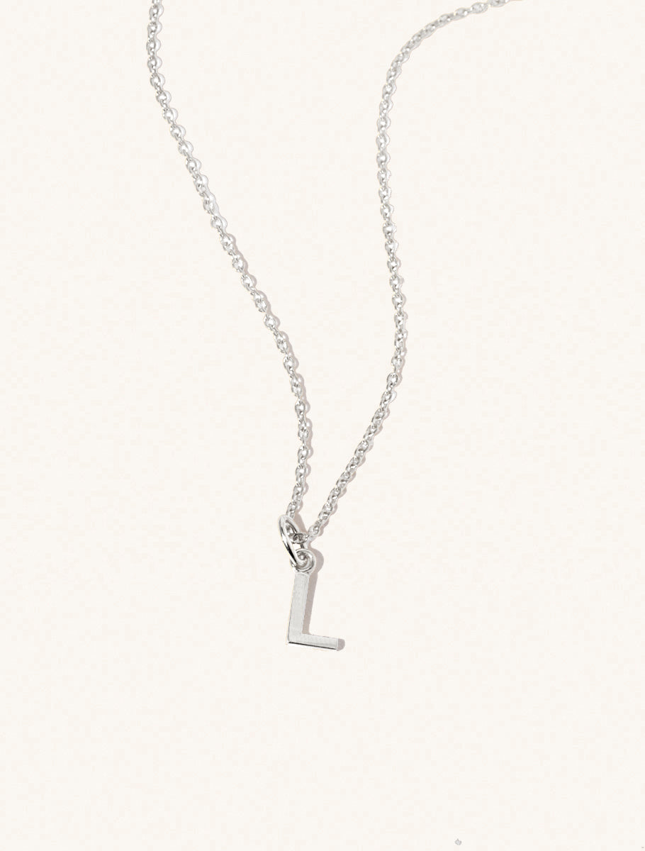 A sterling silver chain necklace with the caplital letter L approximately 8mm x 6mm. Set on a cream background with gentle shadowing.