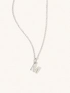 A sterling silver chain necklace with the caplital letter M approximately 8mm x 6mm. Set on a cream background with gentle shadowing.