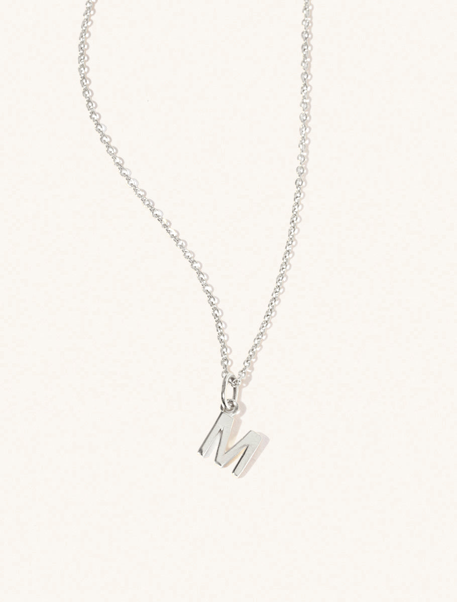 A sterling silver chain necklace with the caplital letter M approximately 8mm x 6mm. Set on a cream background with gentle shadowing.