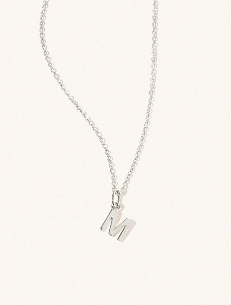 A sterling silver chain necklace with the caplital letter M approximately 8mm x 6mm. Set on a cream background with gentle shadowing.