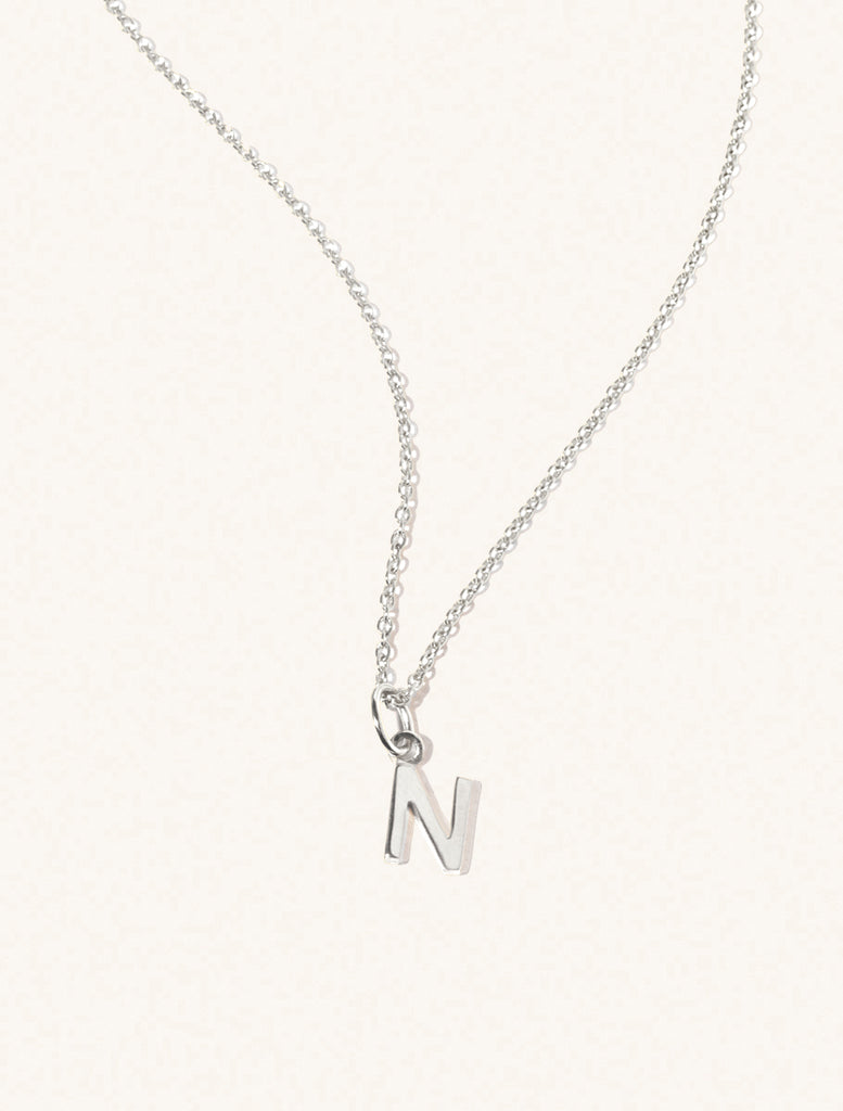 A sterling silver chain necklace with the caplital letter N approximately 8mm x 6mm. Set on a cream background with gentle shadowing.