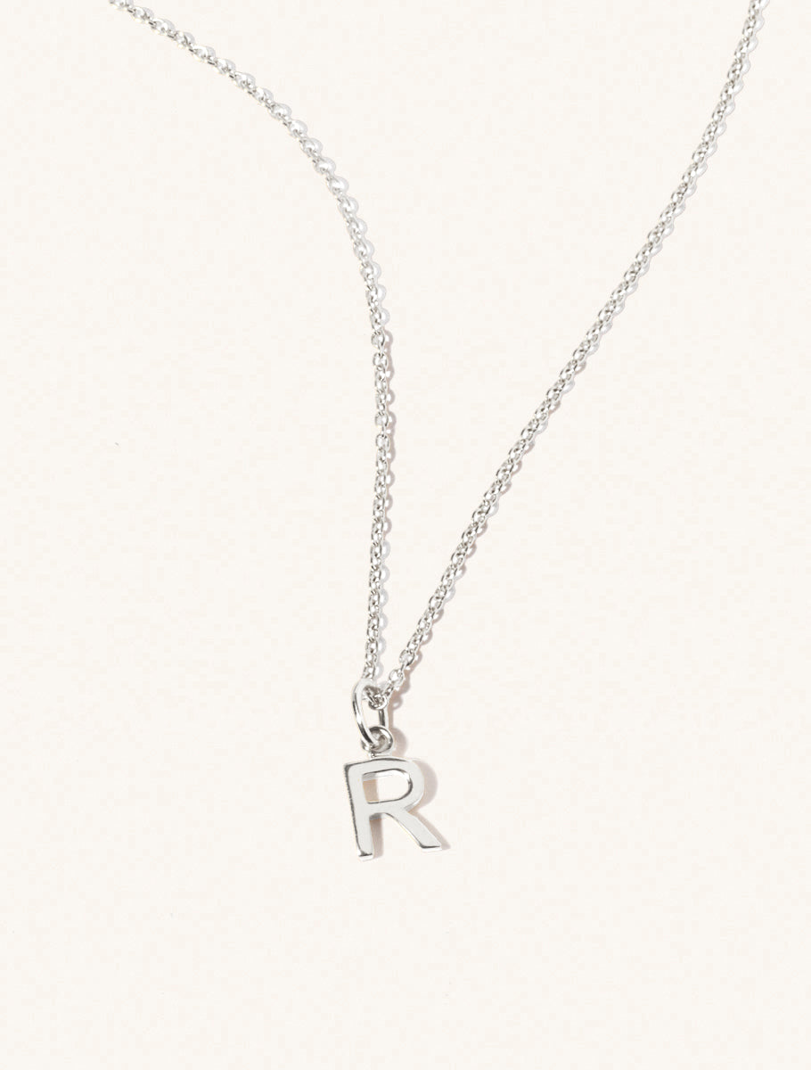 A sterling silver chain necklace with the caplital letter R approximately 8mm x 6mm. Set on a cream background with gentle shadowing.