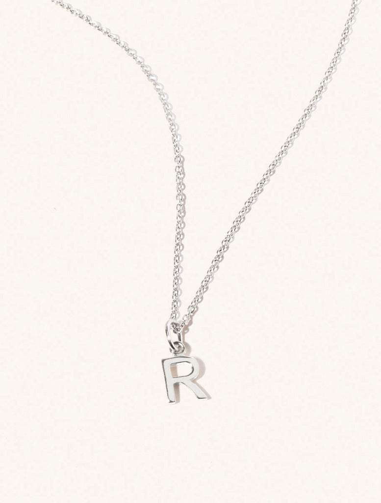 A sterling silver chain necklace with the caplital letter R approximately 8mm x 6mm. Set on a cream background with gentle shadowing.