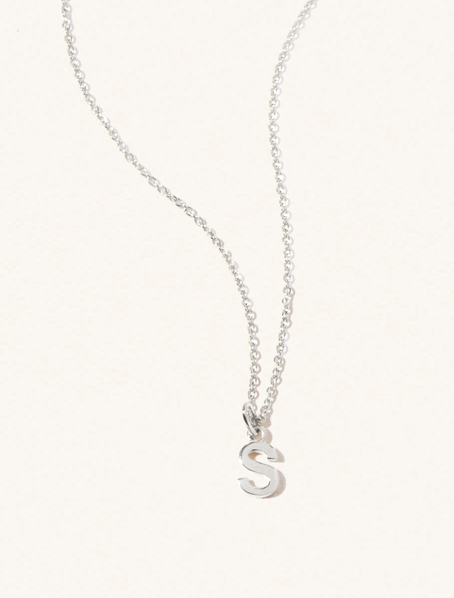 A sterling silver chain necklace with the caplital letter S approximately 8mm x 6mm. Set on a cream background with gentle shadowing.