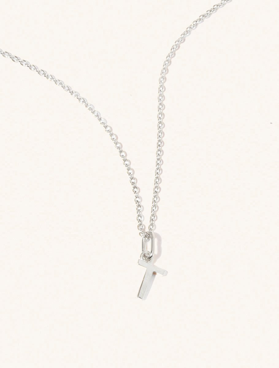 A sterling silver chain necklace with the caplital letter T approximately 8mm x 6mm. Set on a cream background with gentle shadowing.