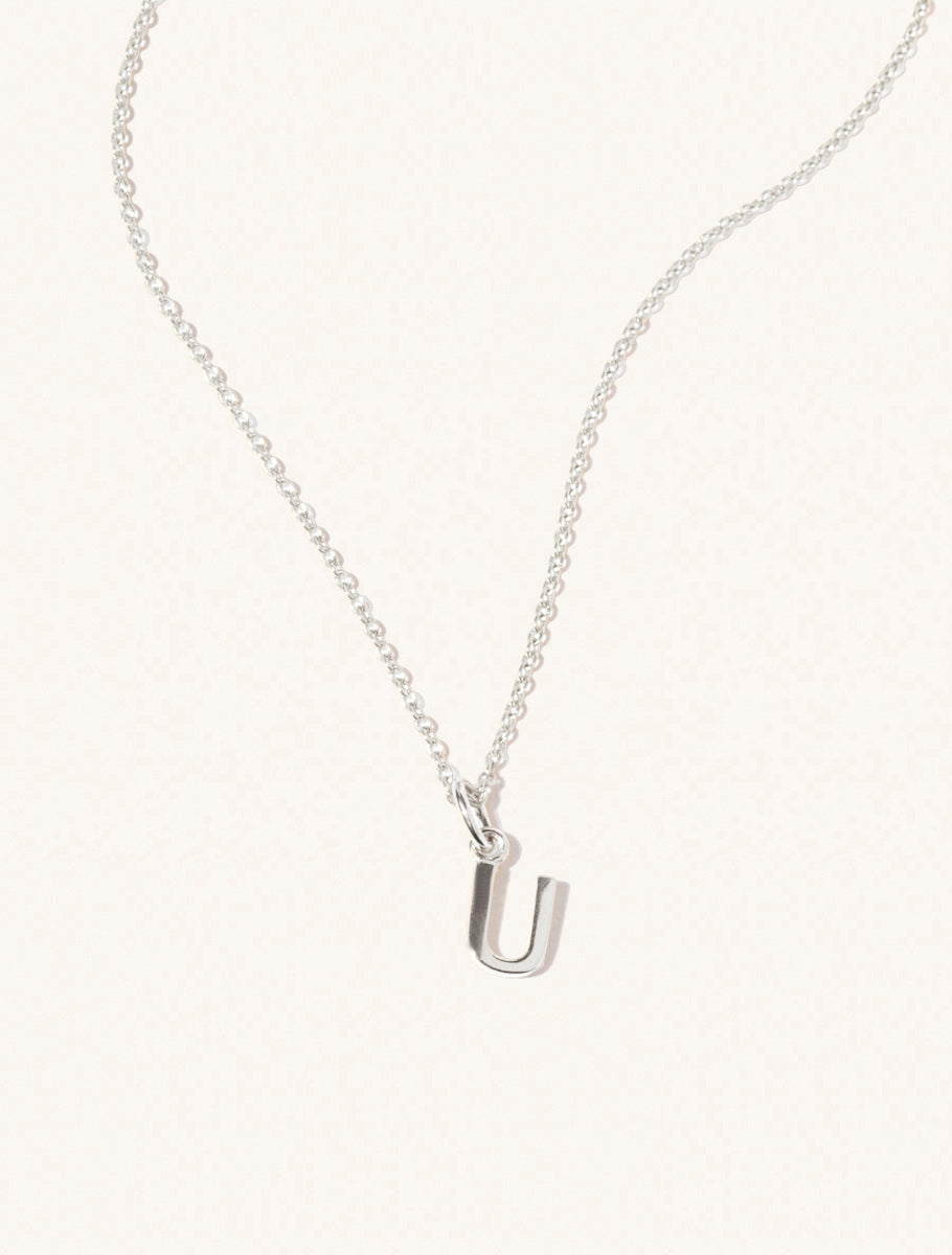 A sterling silver chain necklace with the caplital letter U approximately 8mm x 6mm. Set on a cream background with gentle shadowing.