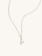 A sterling silver chain necklace with the caplital letter V approximately 8mm x 6mm. Set on a cream background with gentle shadowing.