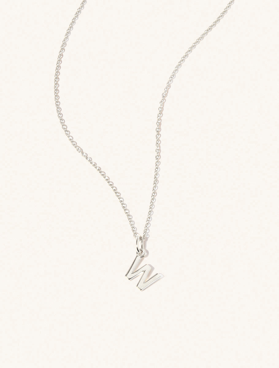 A sterling silver chain necklace with the caplital letter W approximately 8mm x 6mm. Set on a cream background with gentle shadowing.