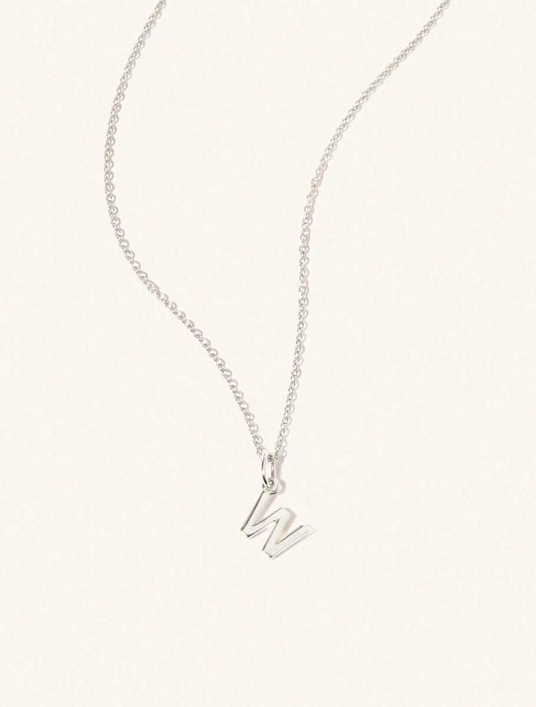 A sterling silver chain necklace with the caplital letter W approximately 8mm x 6mm. Set on a cream background with gentle shadowing.