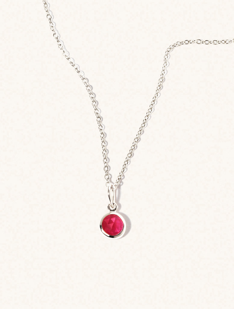 A sterling silver delicate chain nacklace with an 8mm ruby quartz gemstone set in a round pendant. Set on an cream background with gentle shadowing.