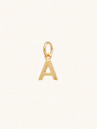 A gold caplital letter A approximately 8mm x 6mm with a connecting ring to thread through a necklace at the top. Set on a cream background.