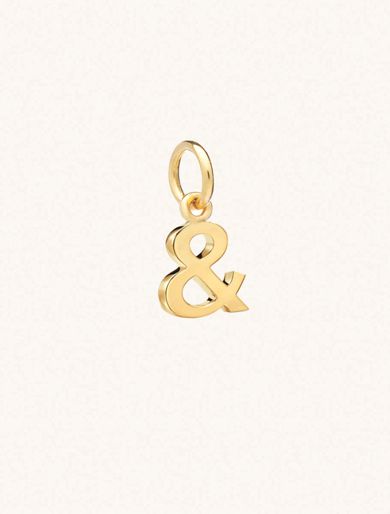 A gold & symbol approximately 8mm x 6mm with a connecting ring to thread through a necklace at the top. Set on a cream background.